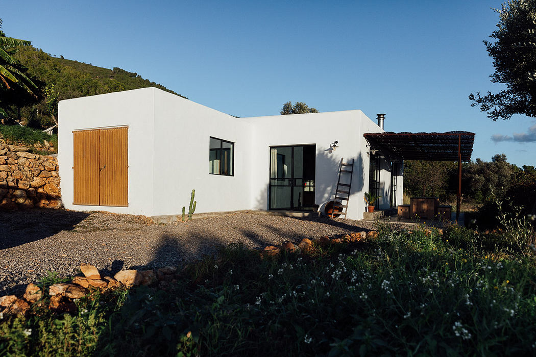 Modern white villa with large windows, set amidst natural landscape.