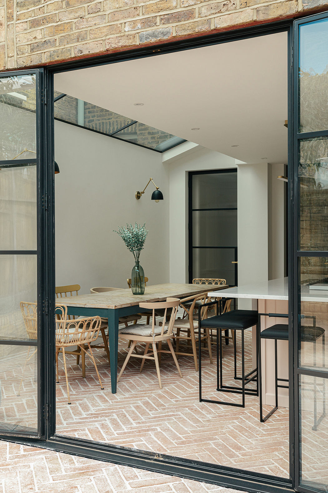 Modern dining area with large glass doors, herringbone brick floor, and natural