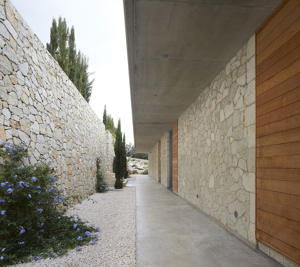 Modern outdoor corridor with stone walls, wooden panels, and gravel path.