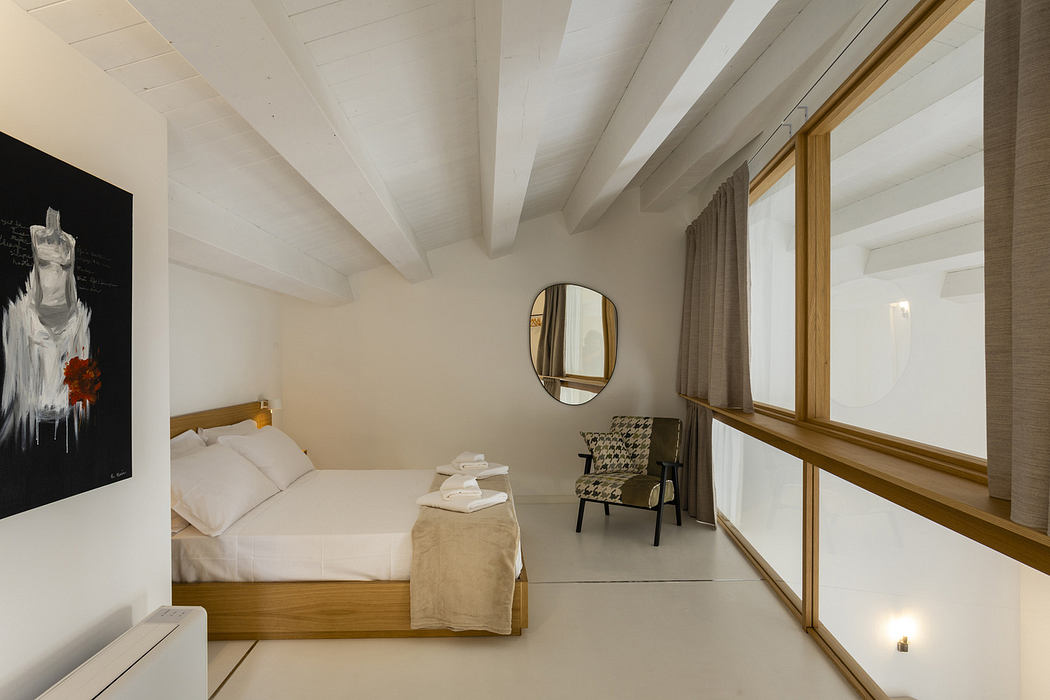 Minimalist bedroom with white decor, exposed beams, and a large window.