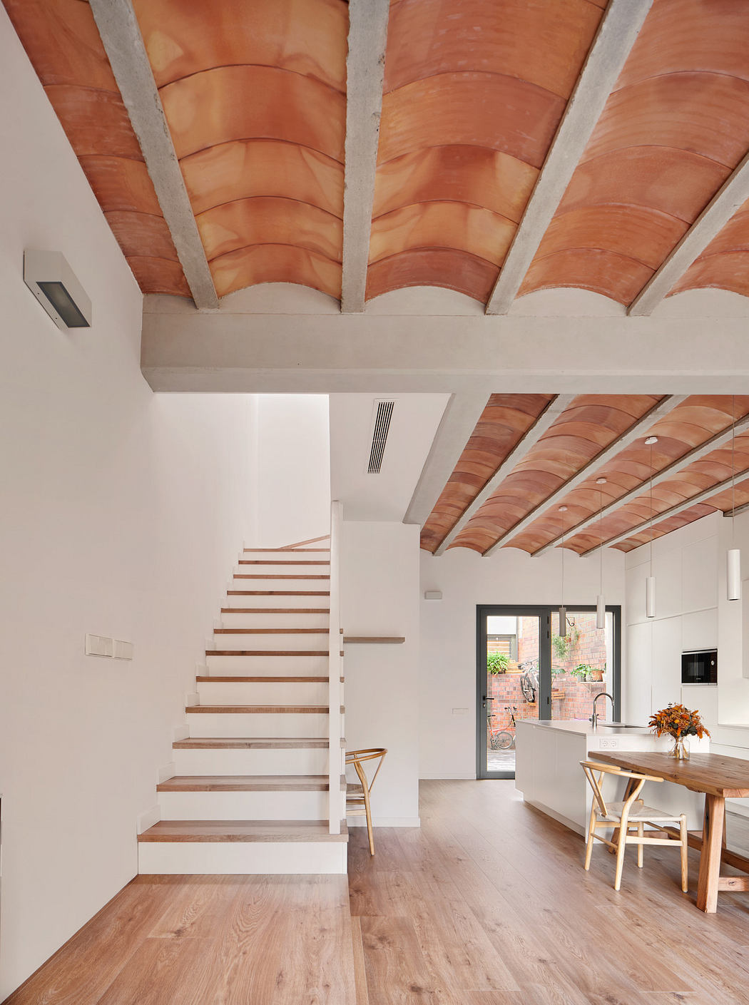 Minimalist interior with wooden stairs and terracotta ceiling vaults.