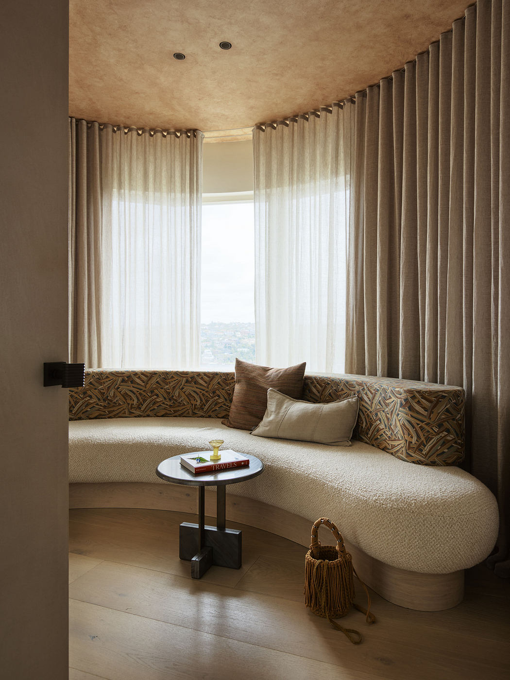 Elegant curved seating nook with patterned cushions, sheer curtains, and a