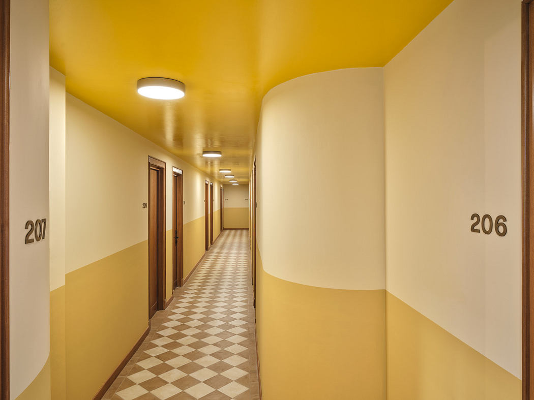 Modern hallway with checkered floor, yellow walls, and numbered doors.
