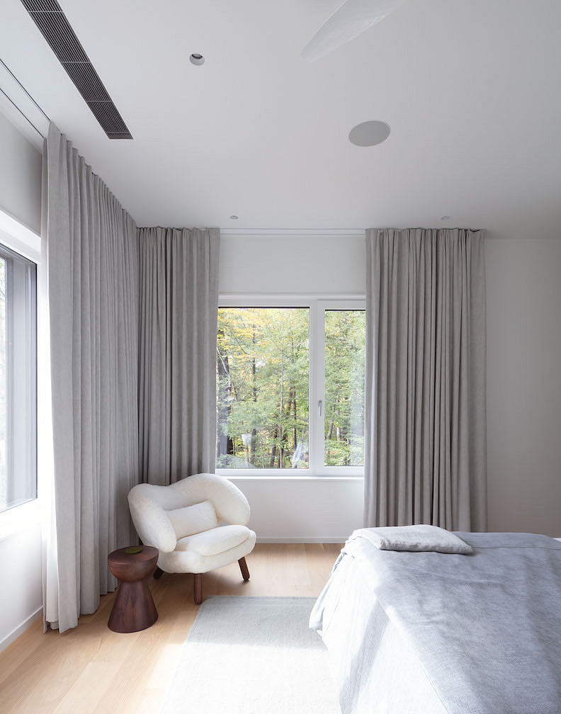 Modern bedroom with large window, white chair, and grey curtains.