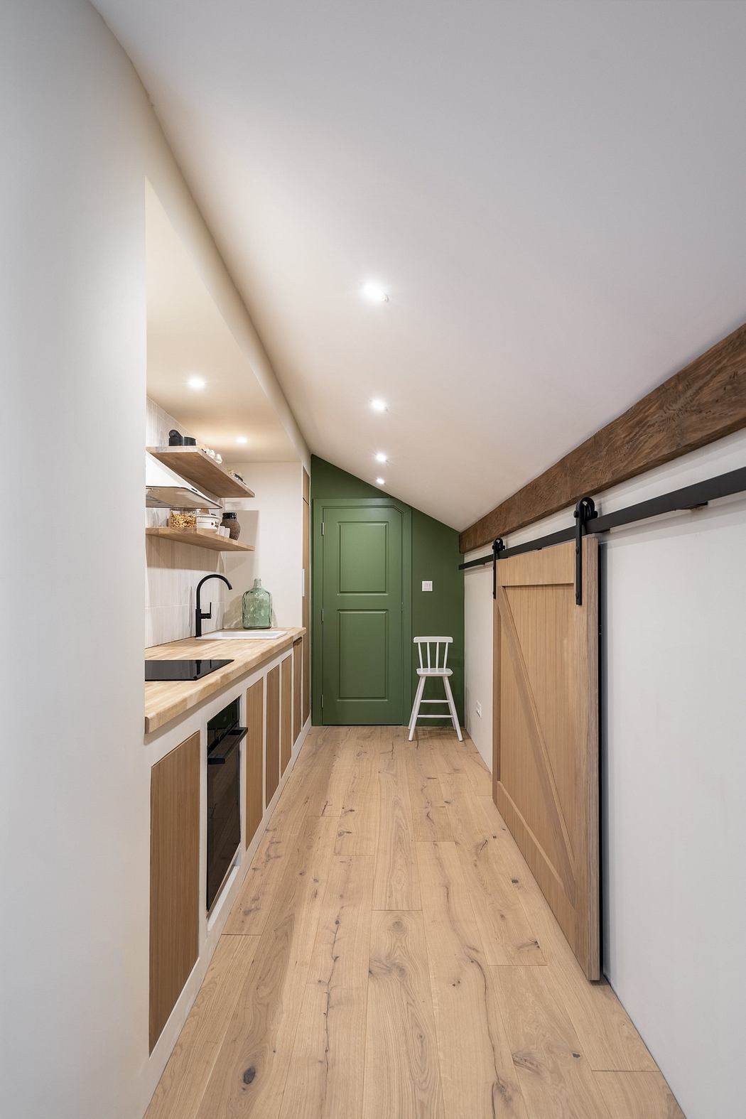 Modern narrow kitchen with wooden countertops and a green door.