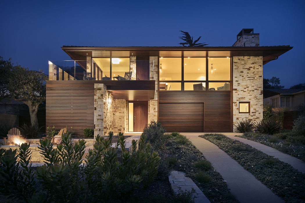 Modern house at dusk with illuminated interiors, large windows, and stone facade.