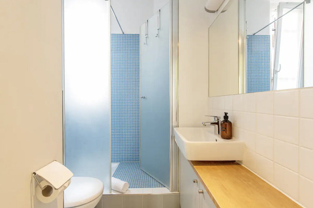 A clean, modern bathroom with a blue tiled shower, white walls, and a