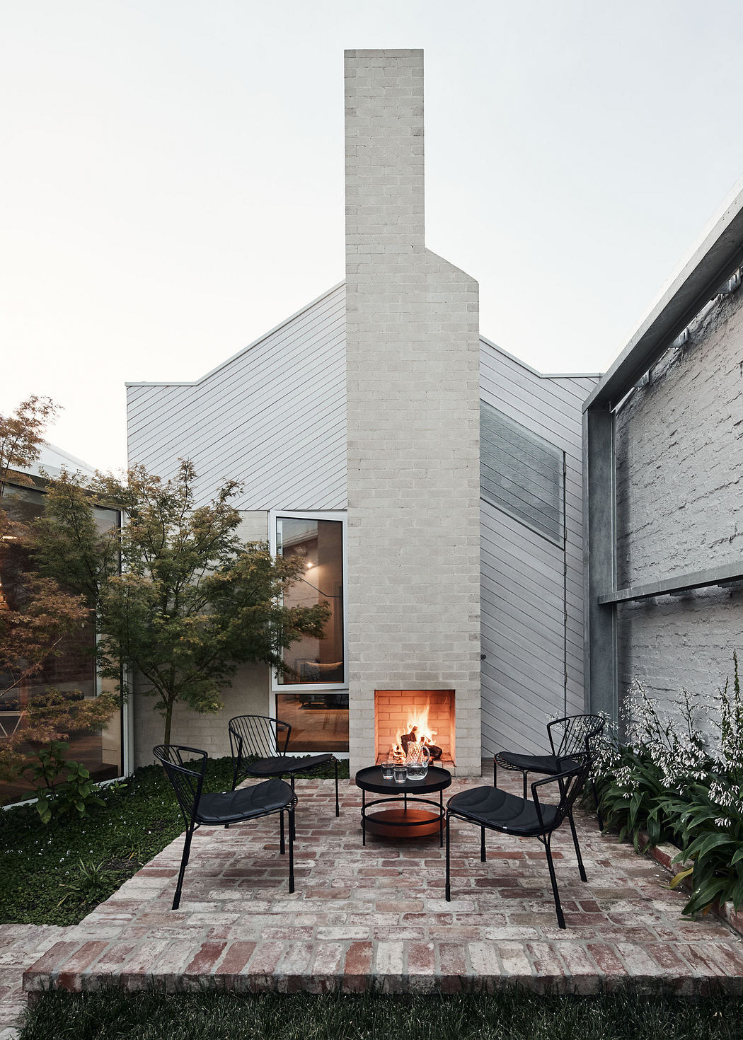 Modern backyard patio with chairs, fire pit, and a tall chimney.