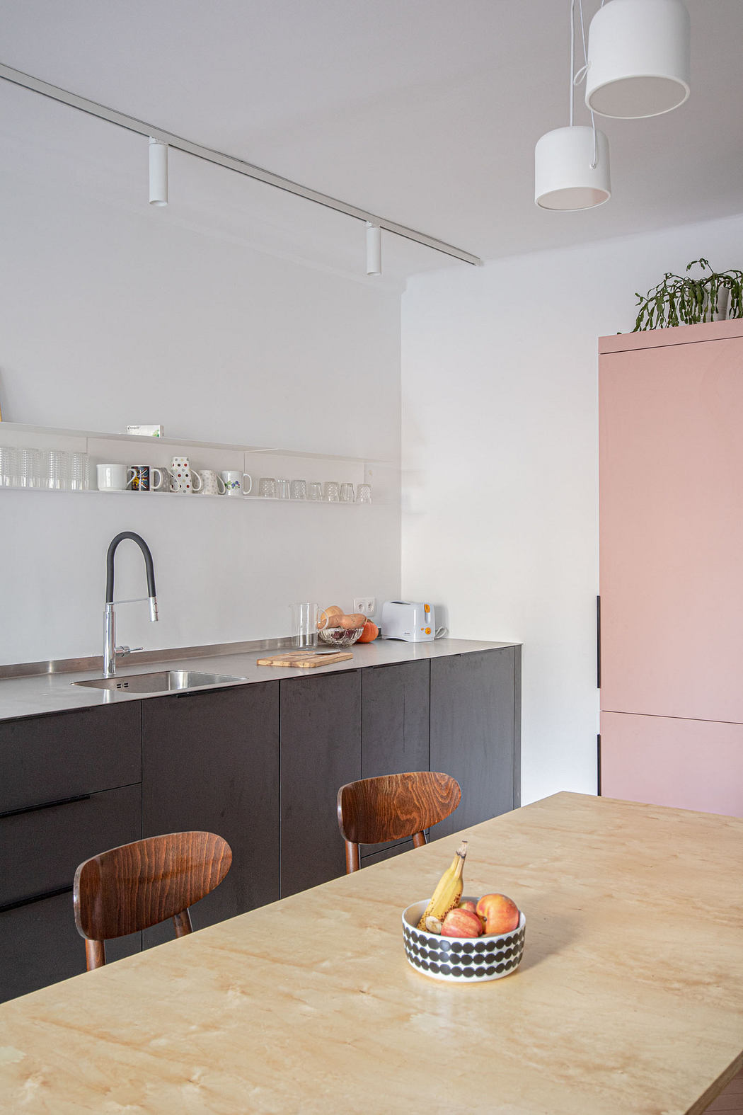 Modern kitchen with pink cabinet, dark counters, and wooden table.