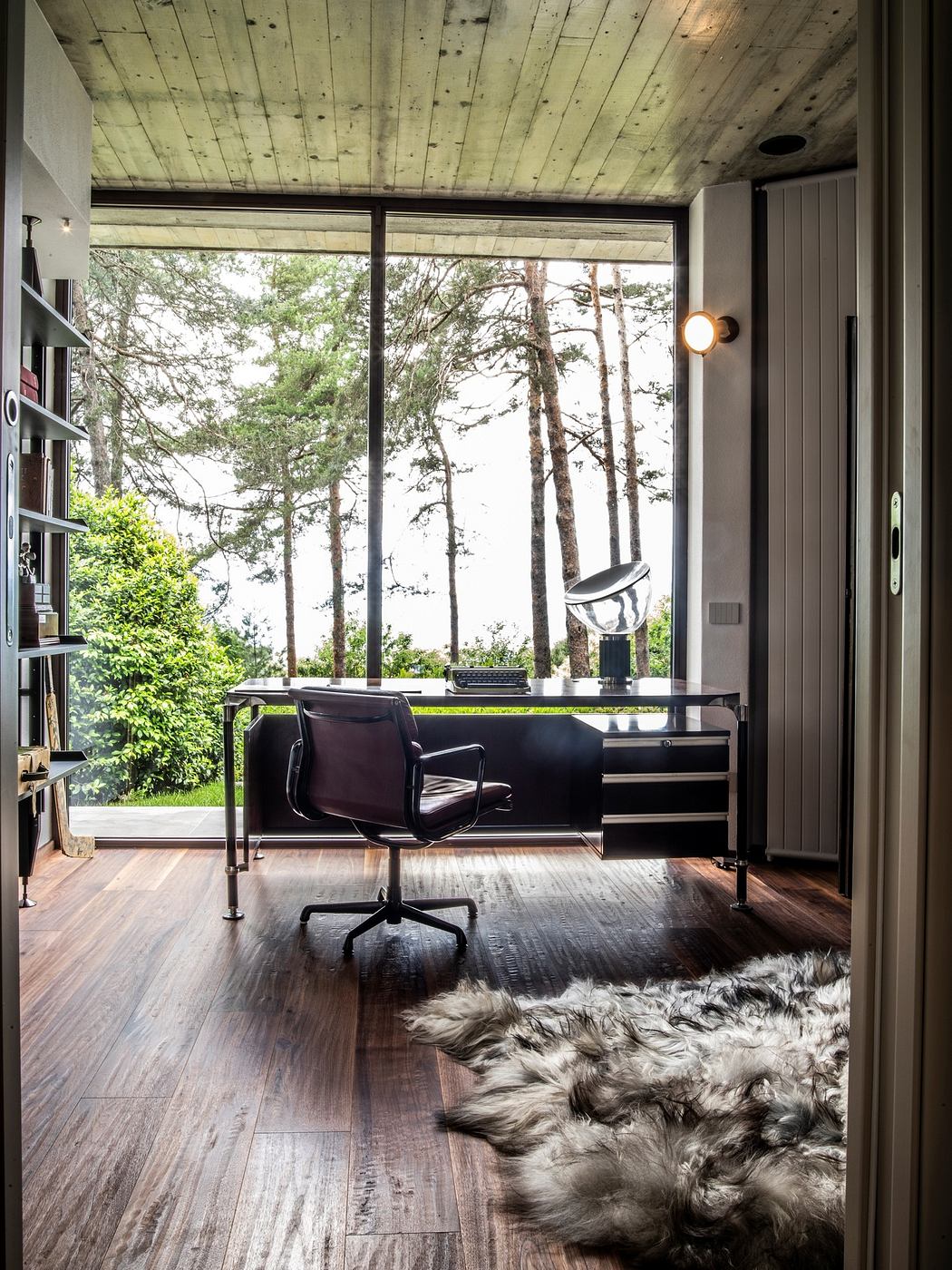 Modern room with large window overlooking trees, hardwood floors, and a fur rug.