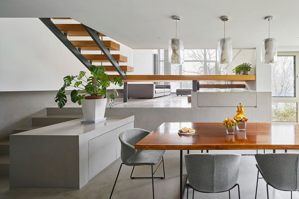 Modern kitchen with wooden dining table, grey chairs, and staircase in background.