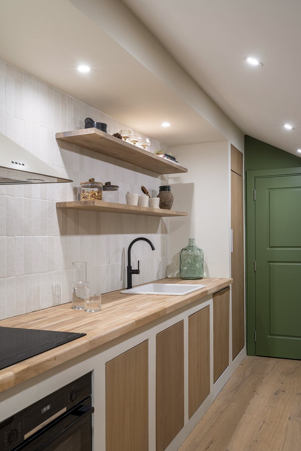 Modern kitchen with wooden countertops, white tiles, and a green door.