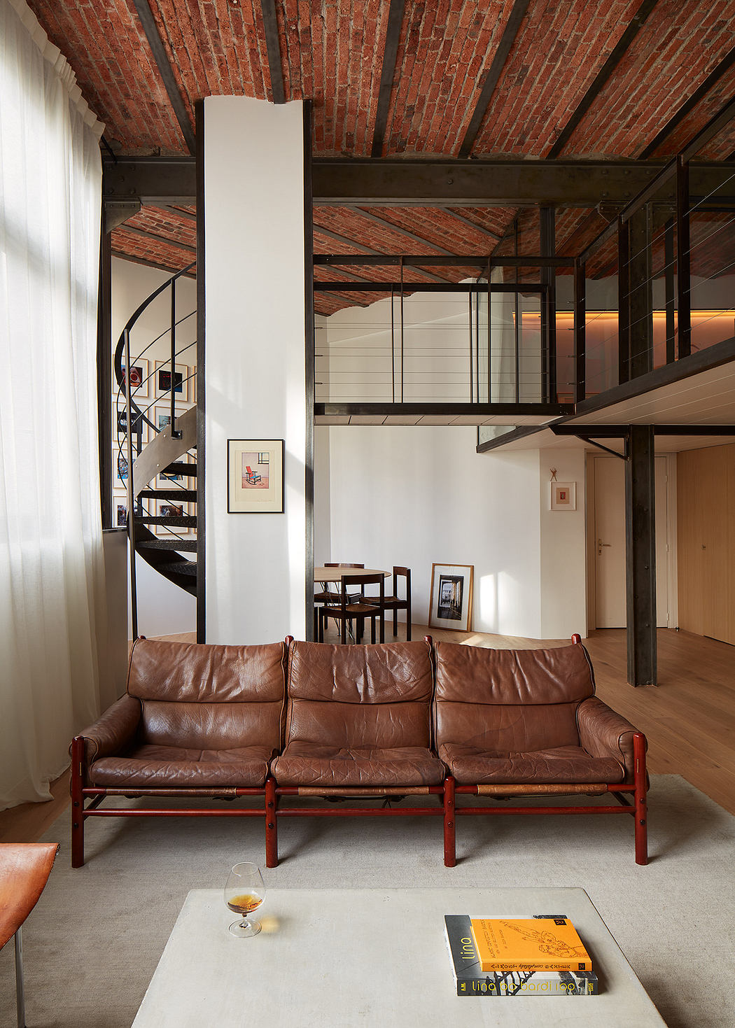 Modern loft interior with exposed brick, spiral staircase, and leather sofa.