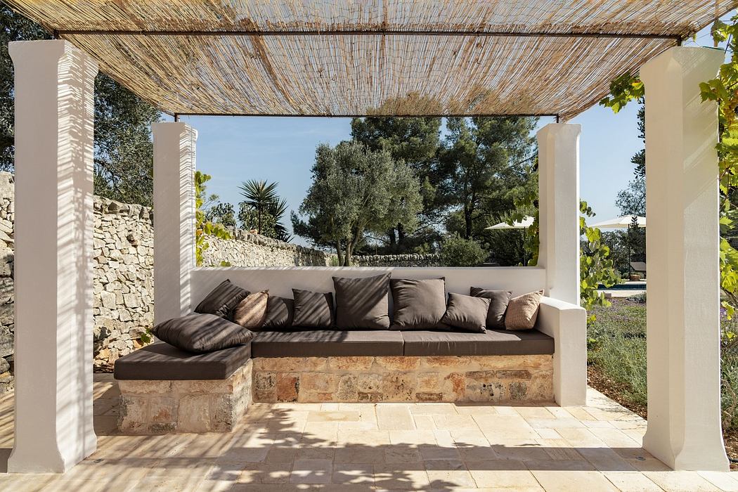Outdoor patio with stone bench, cushions, and wooden pergola.