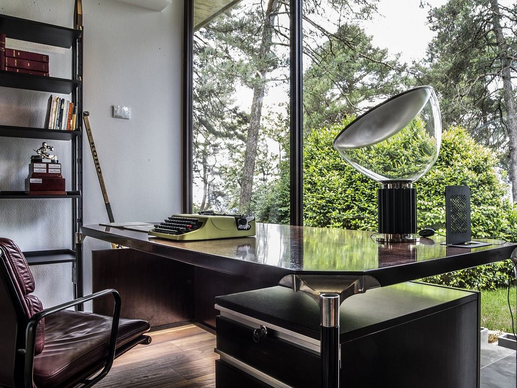Modern home office with sleek black desk, designer lamp, and large window with forest
