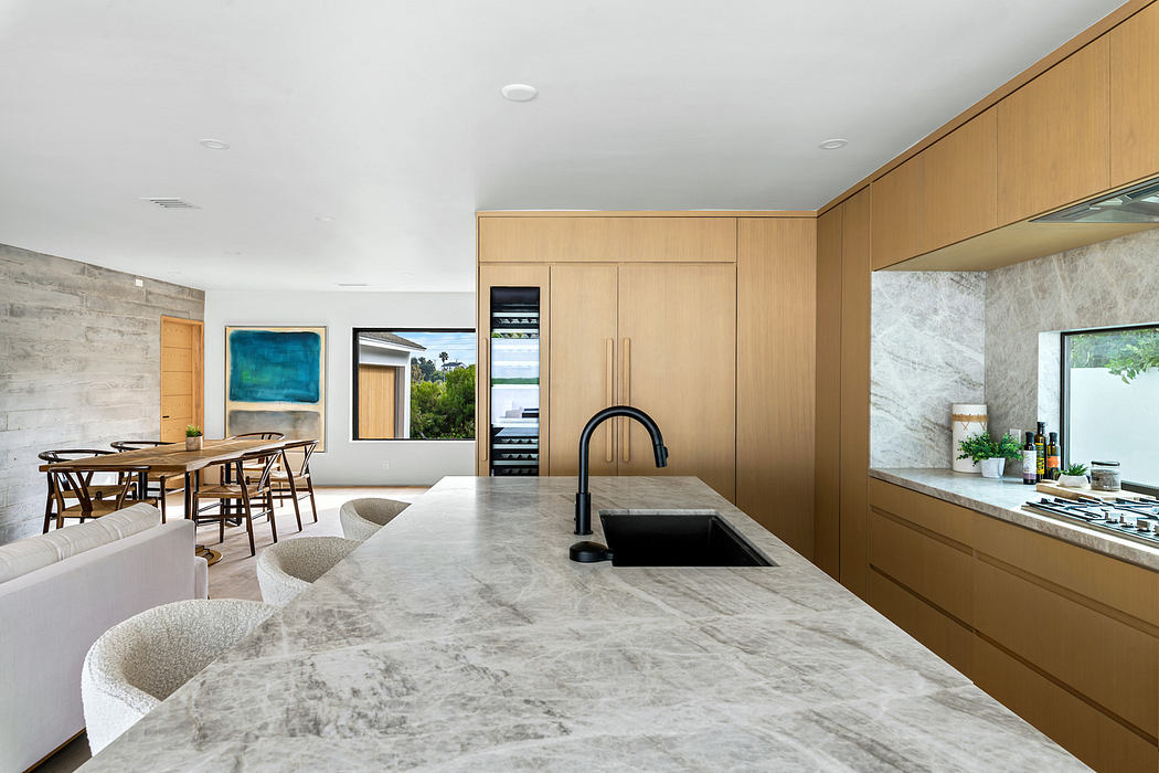 Modern kitchen with a marble island, wood cabinets, and dining area in the background