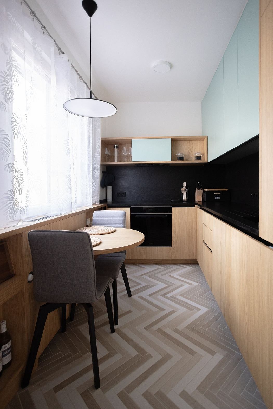 Modern kitchen interior with light wood cabinets and chevron floor.