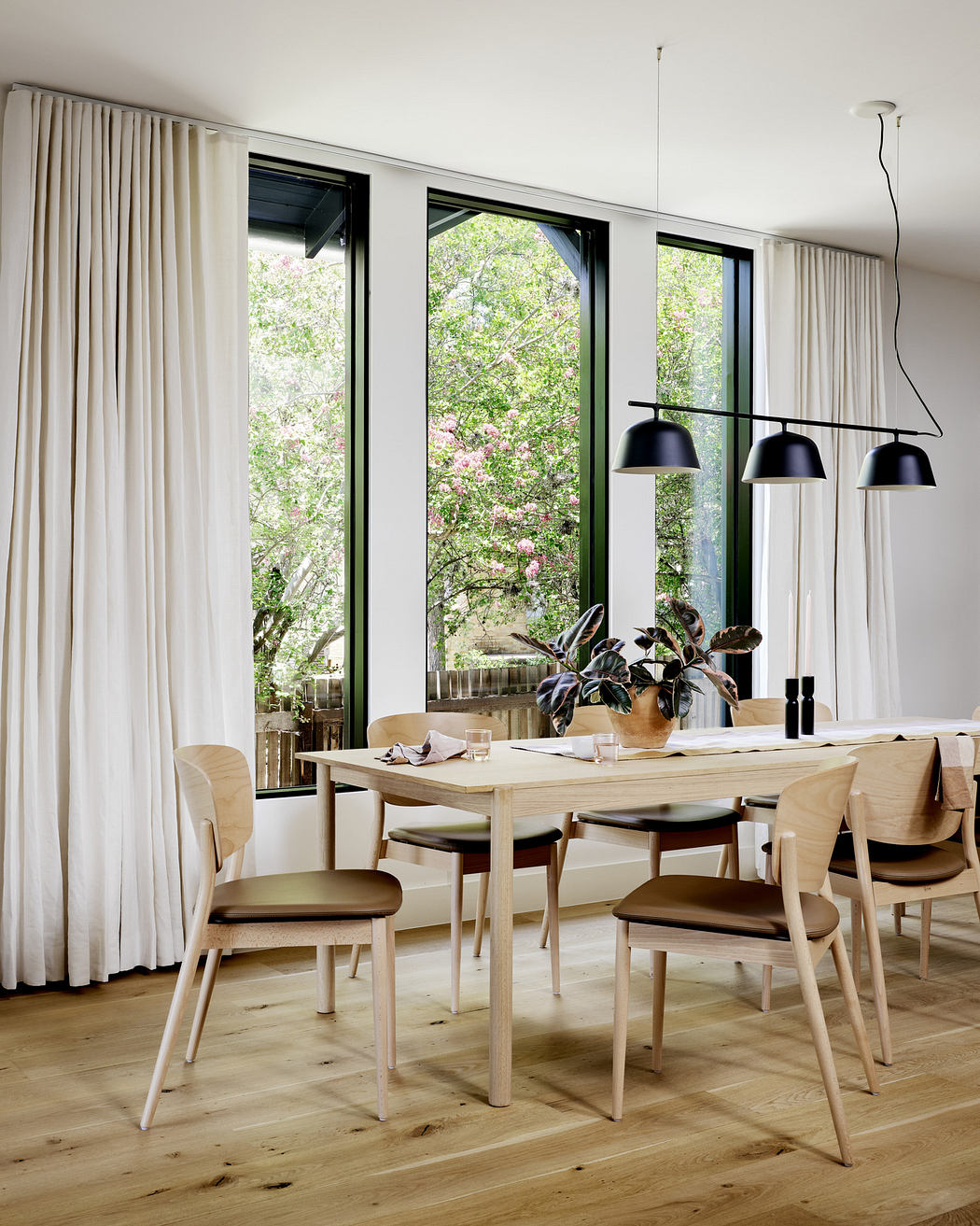 Modern dining room with large windows, wooden table, chairs, and pendant lights.