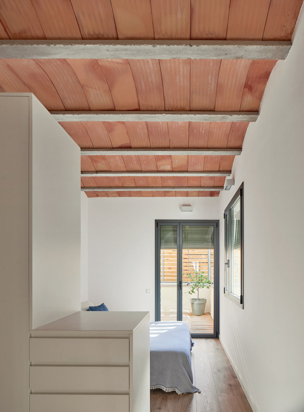 Minimalist bedroom with terracotta ceiling beams, white walls, and a door