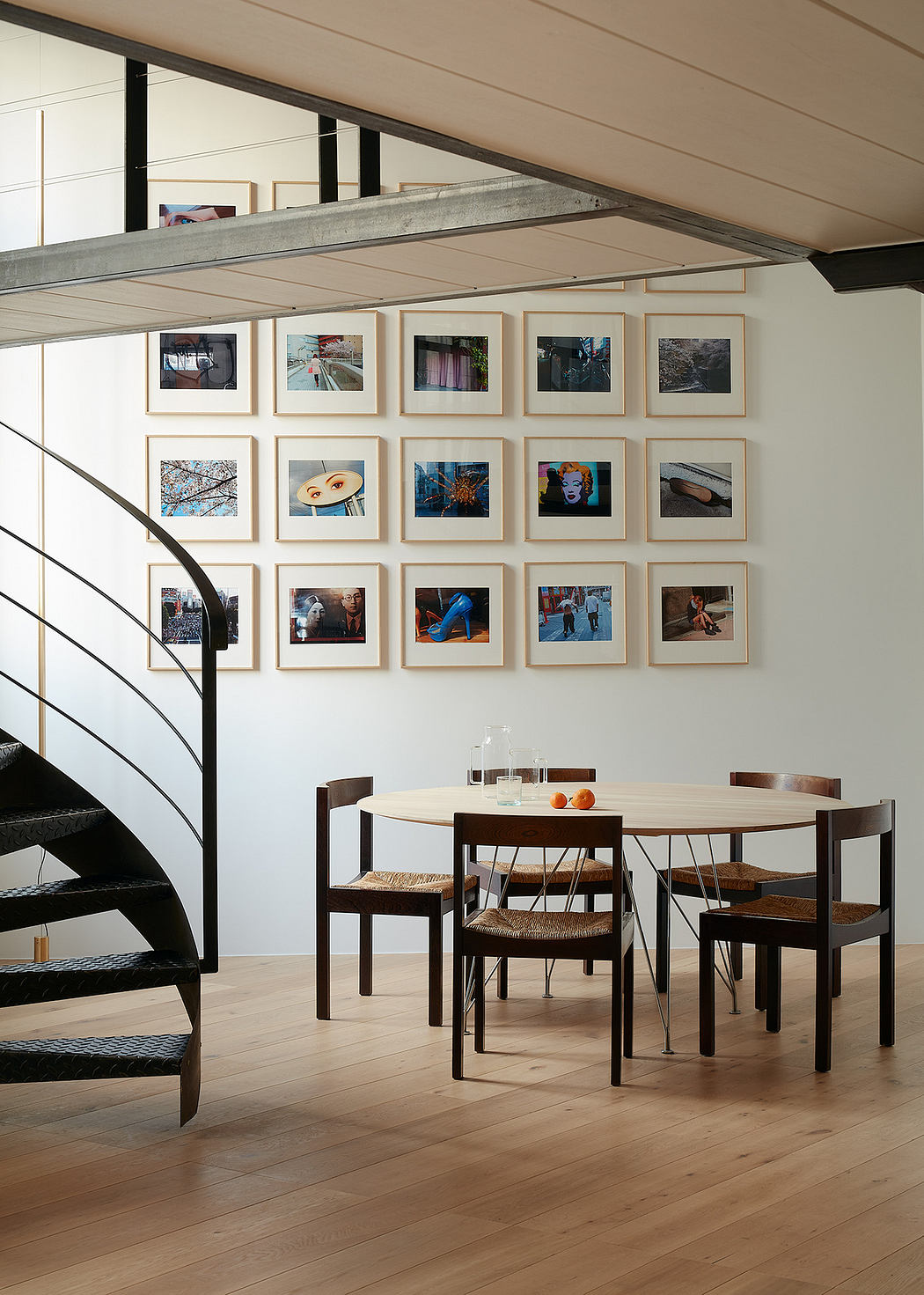 Modern dining room with a wooden table, chairs, gallery wall, and spiral staircase
