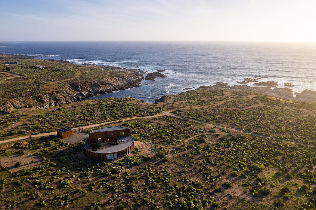 Aerial view of a circular modern house near a rugged coastline.