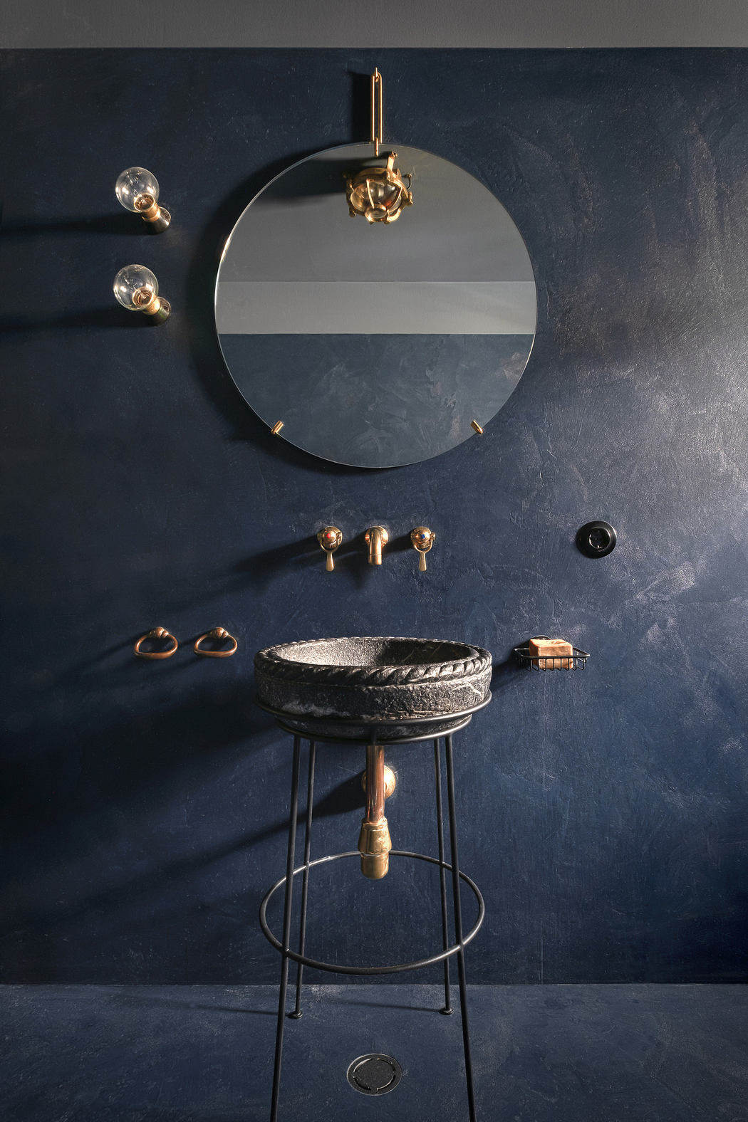 Elegant bathroom with dark blue walls, round mirror, and stylish accessories.