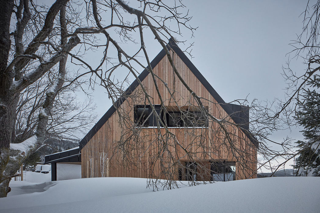 Modern wooden cabin in a snowy landscape with bare trees.