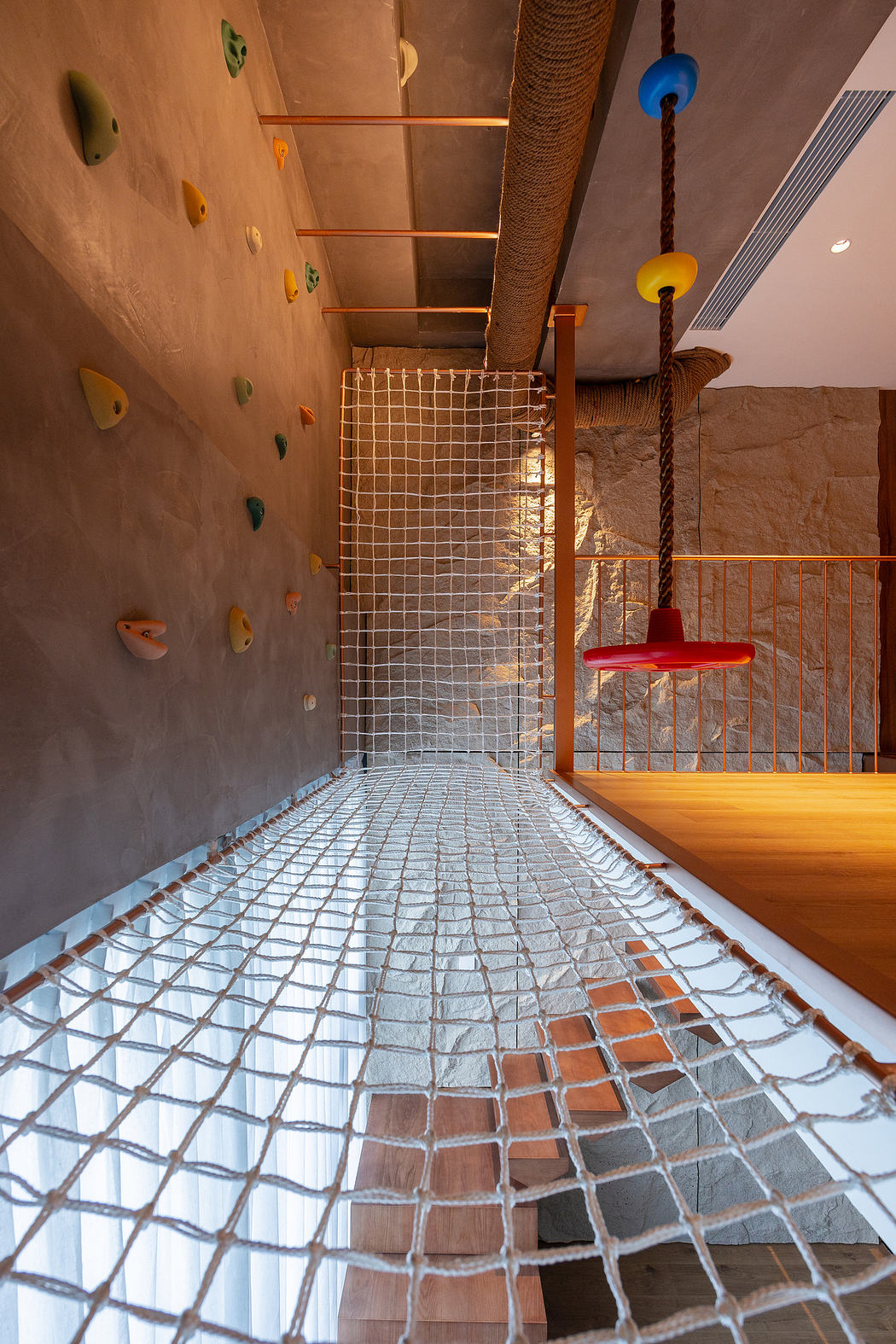 Interior view of a playroom with climbing wall and net bridge.