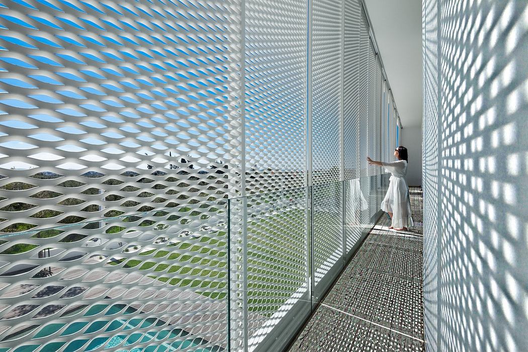 Woman in white dress on a balcony with patterned perforated walls, creating light