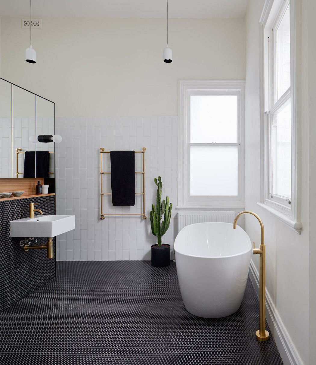 Modern bathroom with white freestanding tub, black hexagonal tiles, and gold