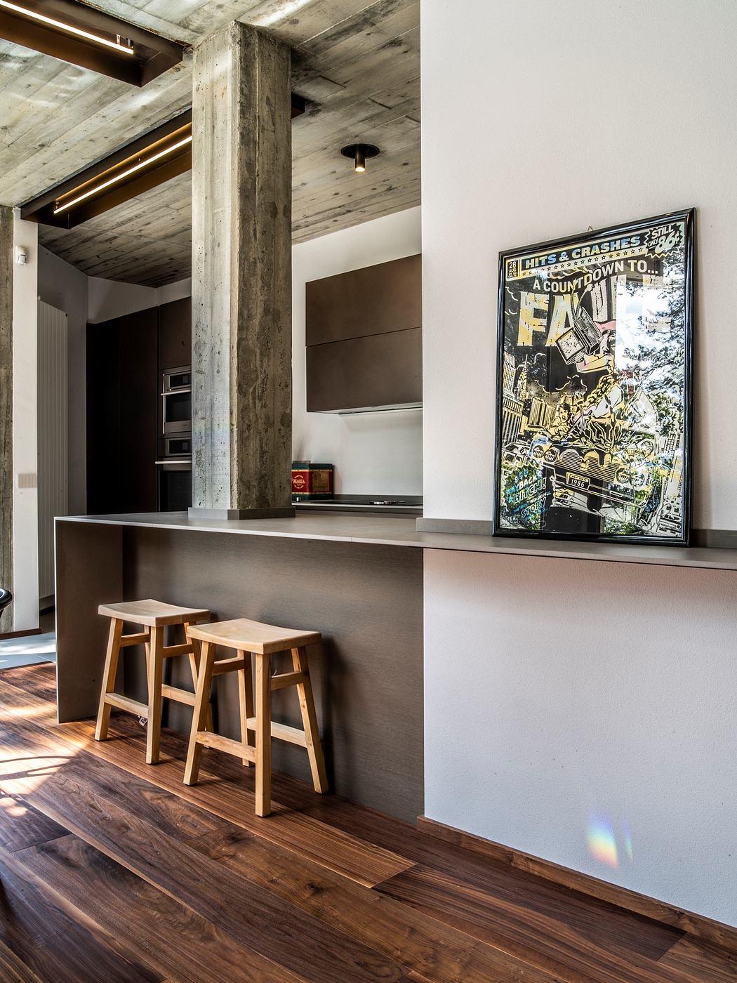 Modern kitchen corner with wooden stools, exposed concrete, and framed artwork.
