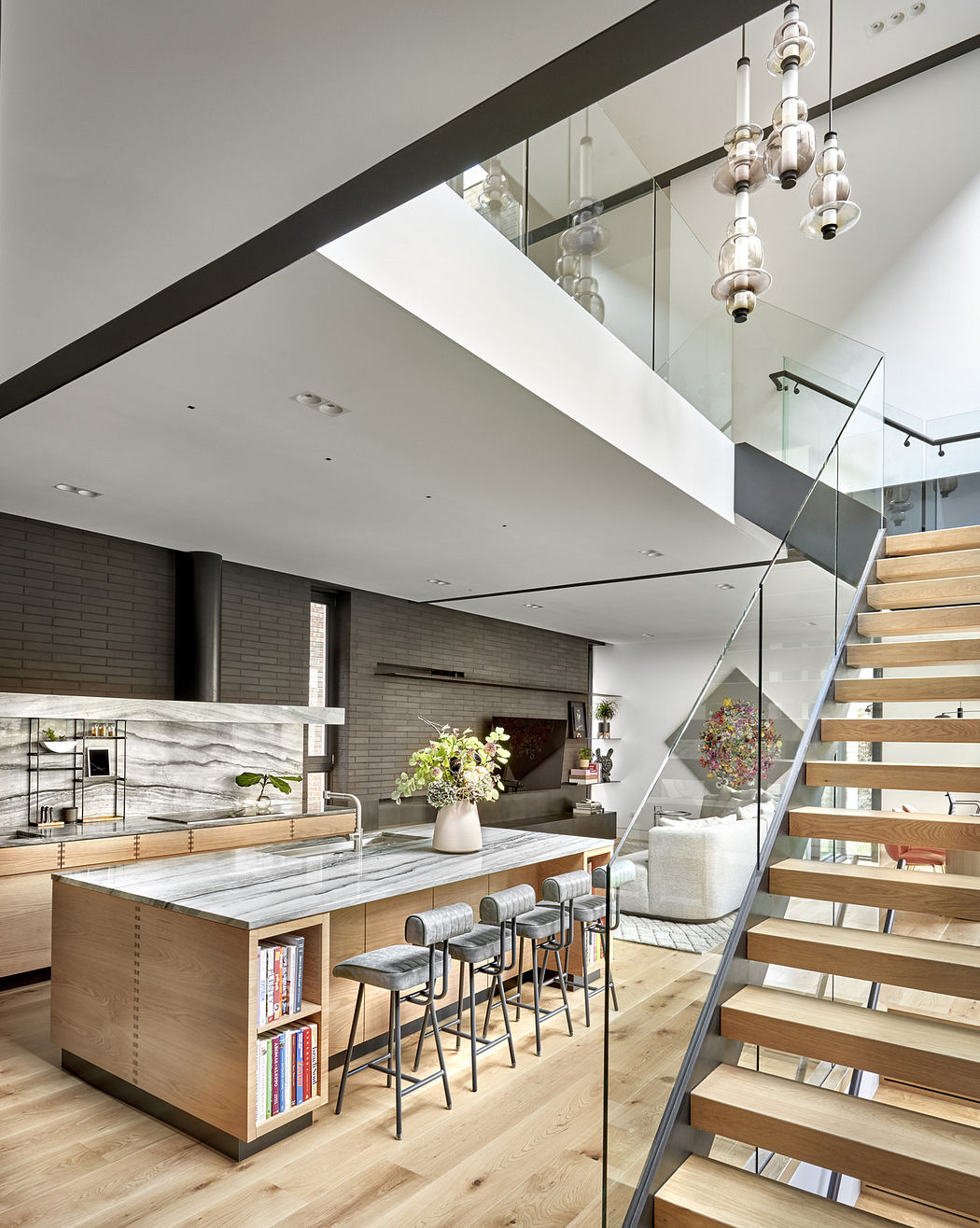 Modern home interior with wooden stairs, glass railing, and an open-plan kitchen.