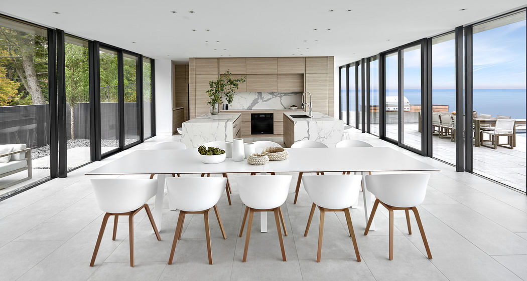 Modern dining room with large white table, chairs, and panoramic windows overlooking the sea