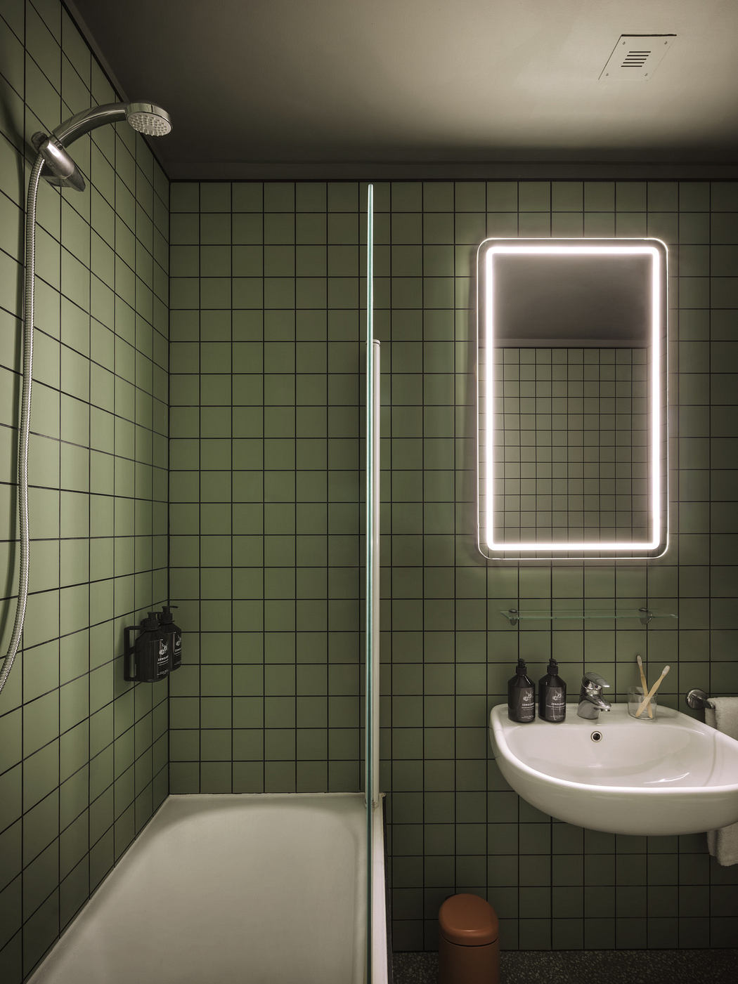 Modern bathroom with green tile, illuminated mirror, and white fixtures.