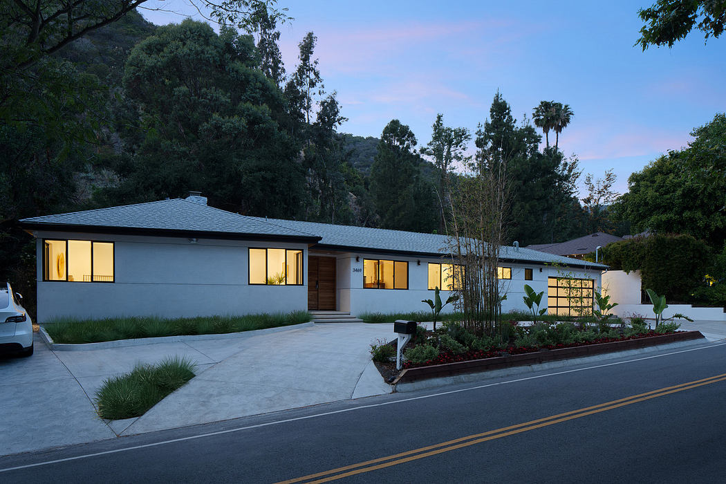 Modern single-story house at dusk with illuminated windows and landscaped front yard.