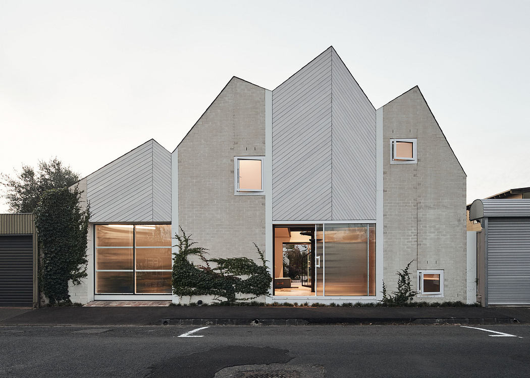 Modern house with peaked roofs and illuminated interior at dusk.