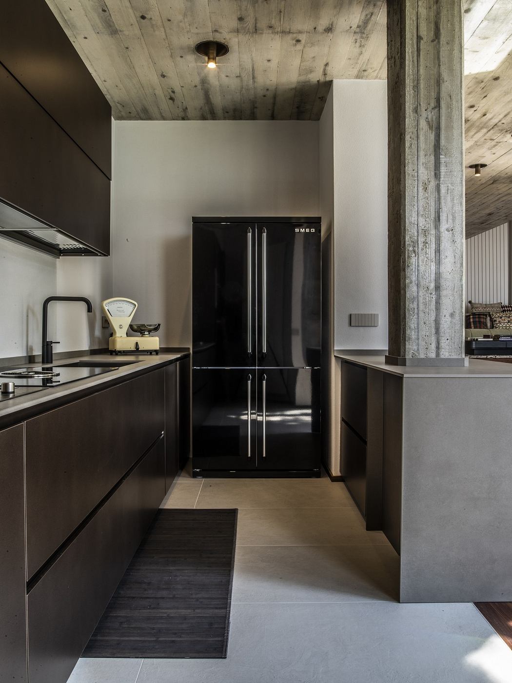 Modern kitchen with dark cabinets, concrete pillars, and a sleek black refrigerator.