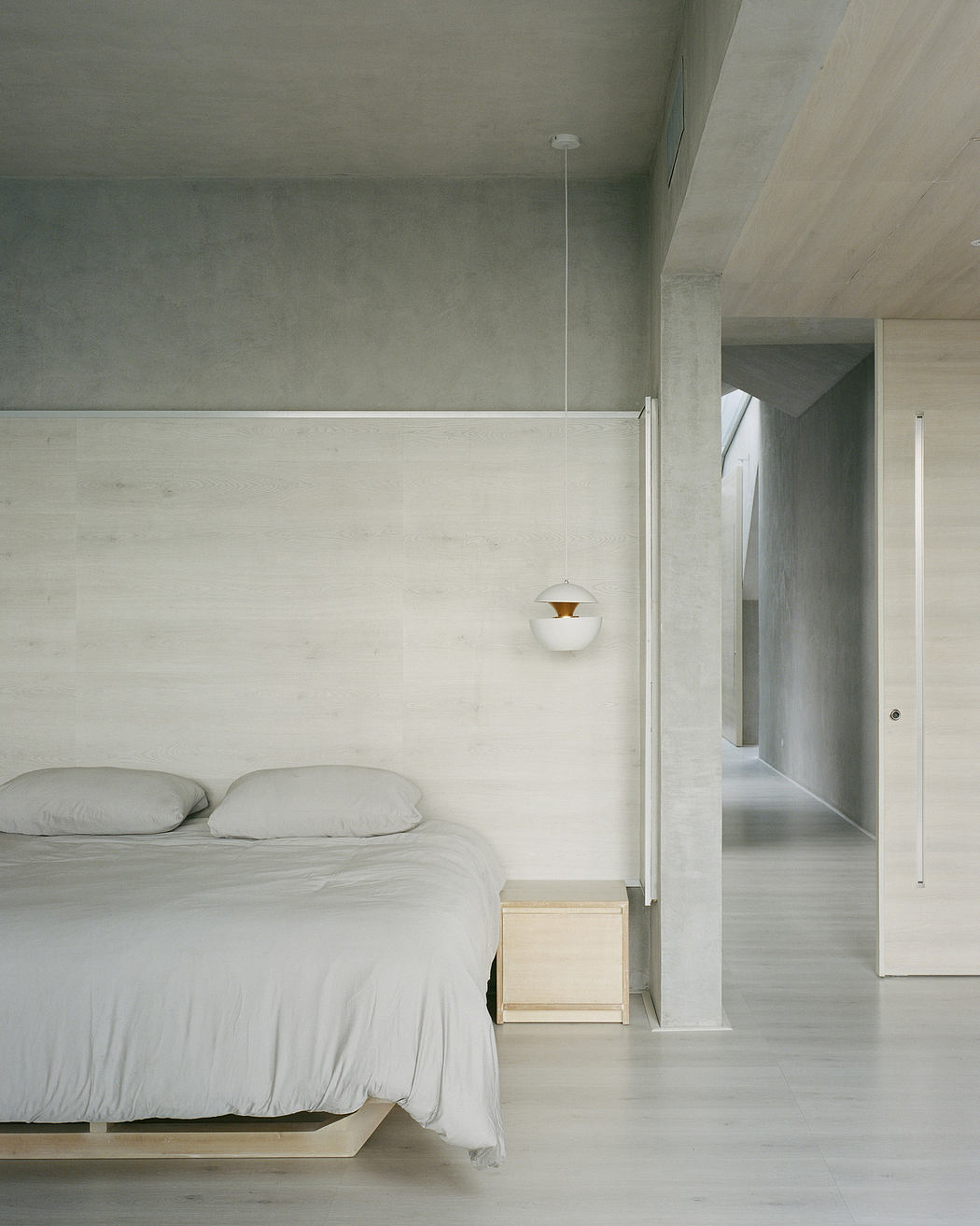 Minimalist bedroom with concrete walls, wooden accents, and simple bedding.