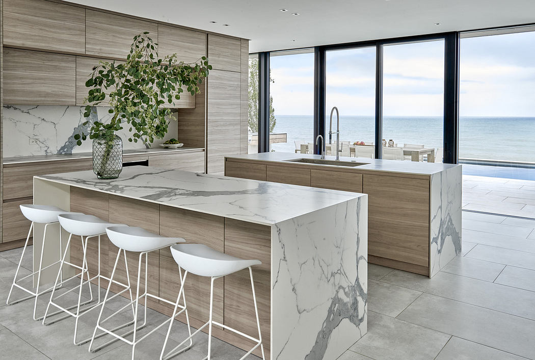 Modern kitchen with marble island, white stools, and ocean view.