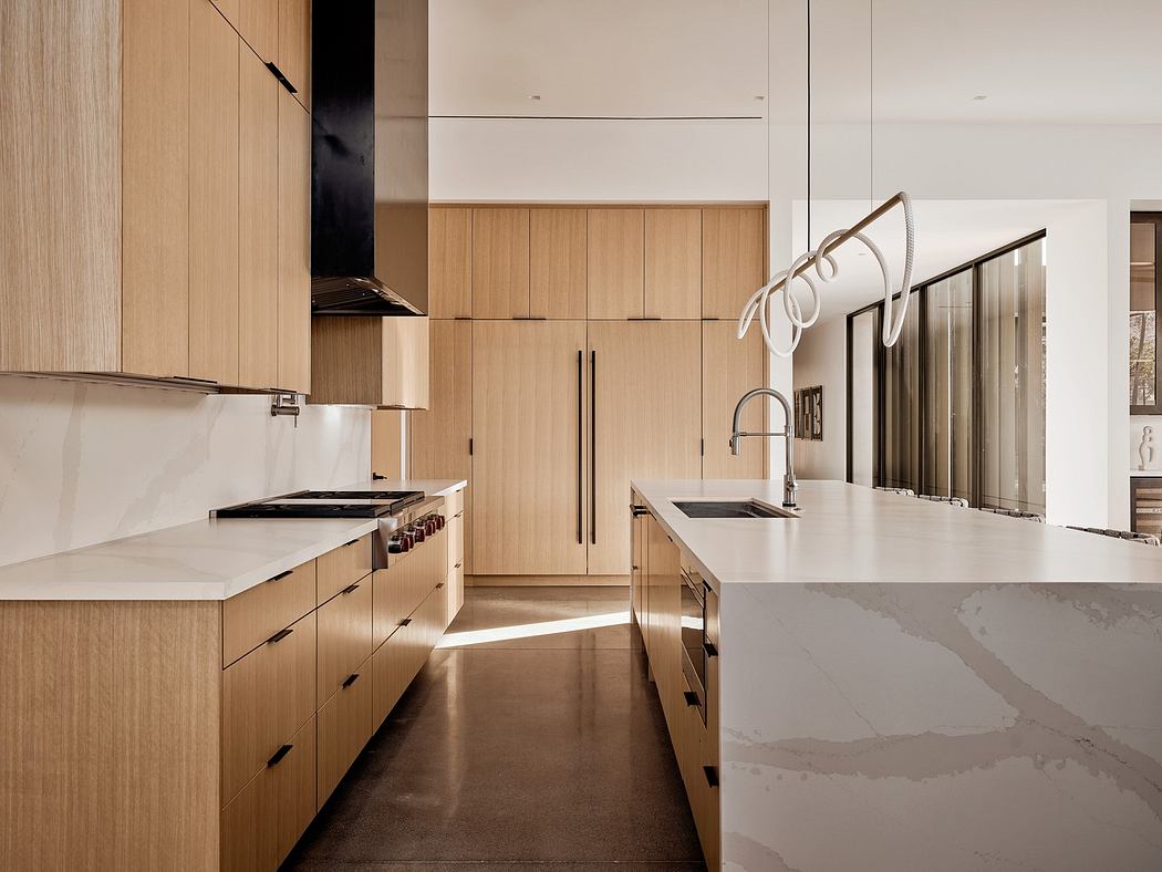 Modern kitchen with light wood cabinets and marble countertops.