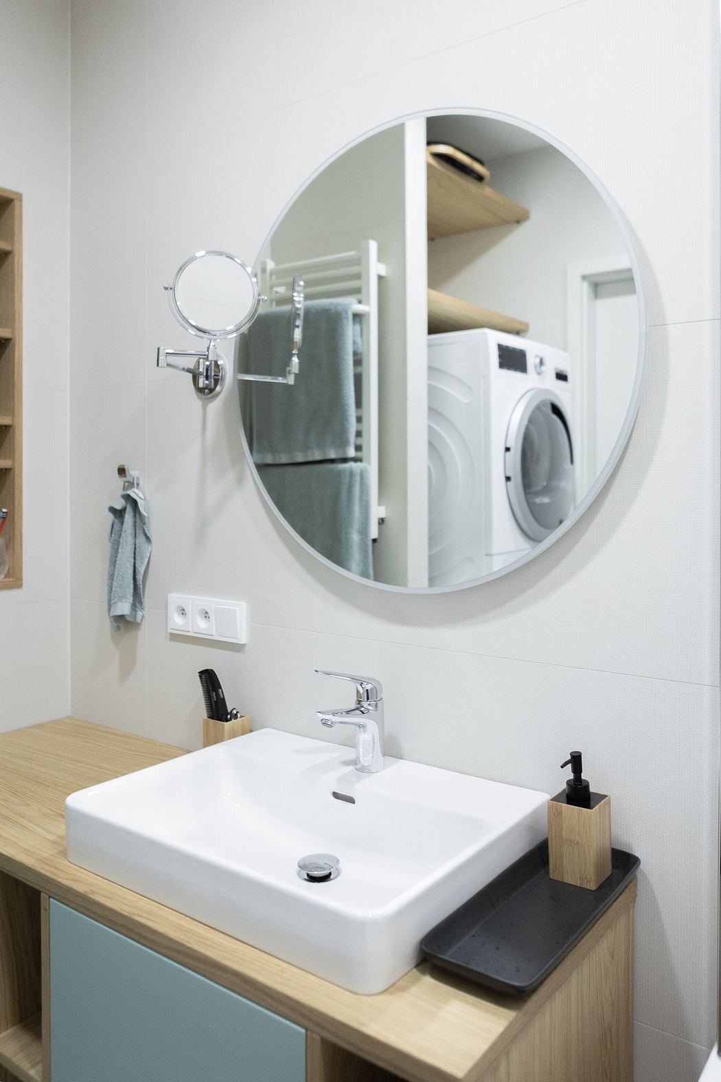 Modern bathroom with a round mirror, sink, and visible laundry area.