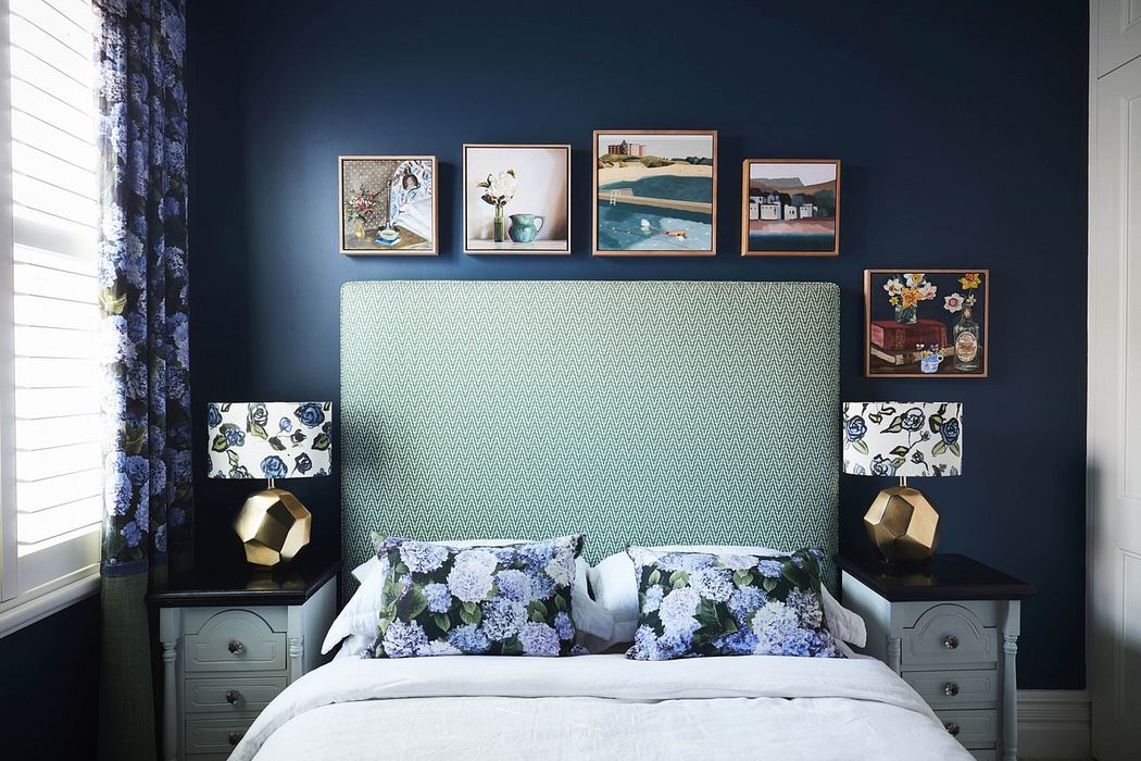 Elegant bedroom with navy walls, patterned headboard, and framed art above
