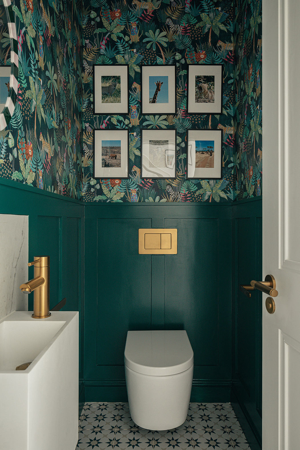 Small bathroom with tropical wallpaper, green wainscoting, and gold fixtures.