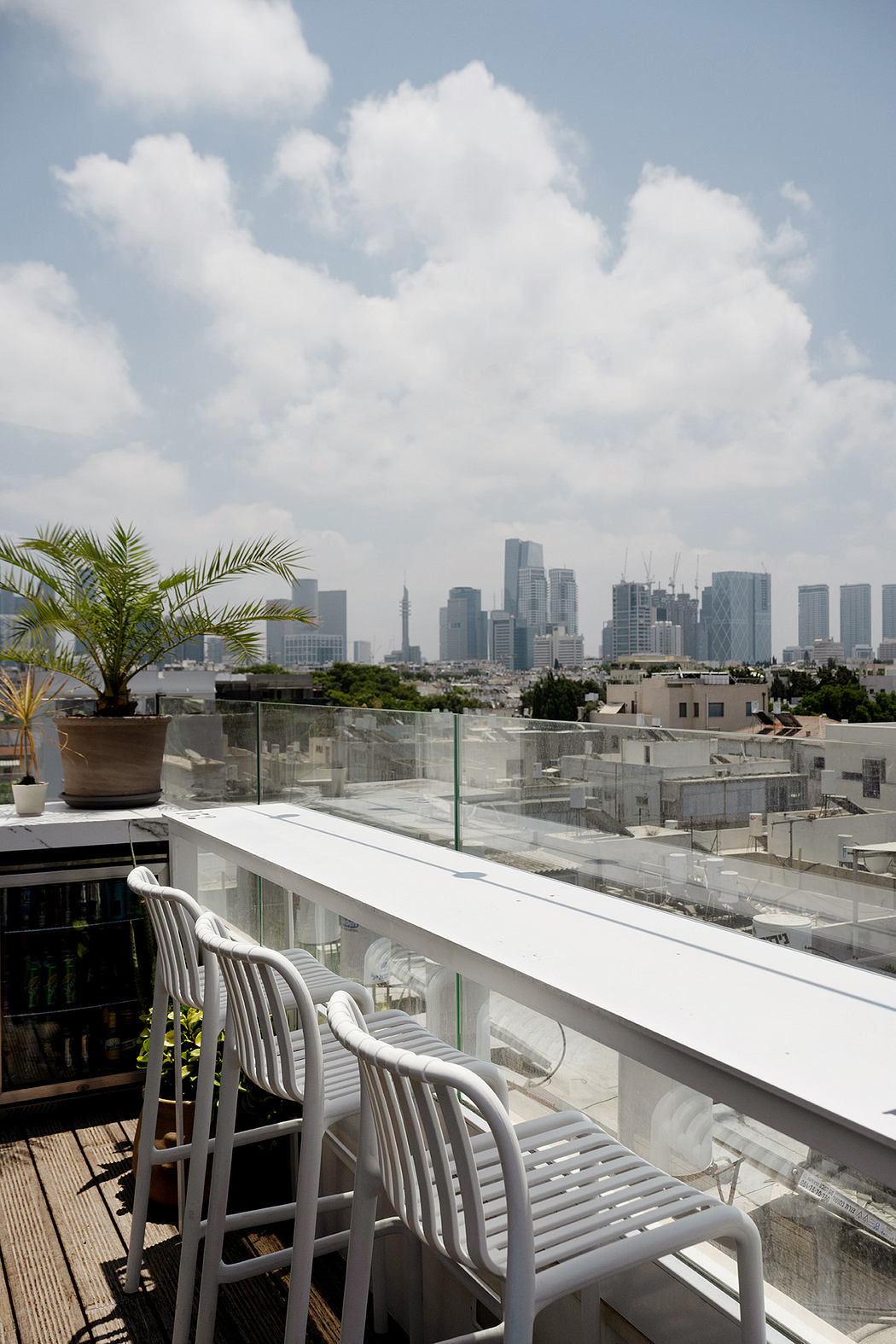 Rooftop patio with white chairs overlooking a city skyline.