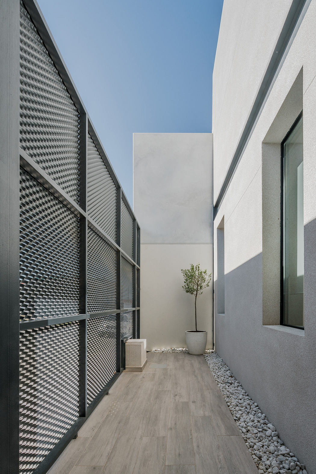 Modern exterior corridor with mesh paneling and minimalistic plant decor.