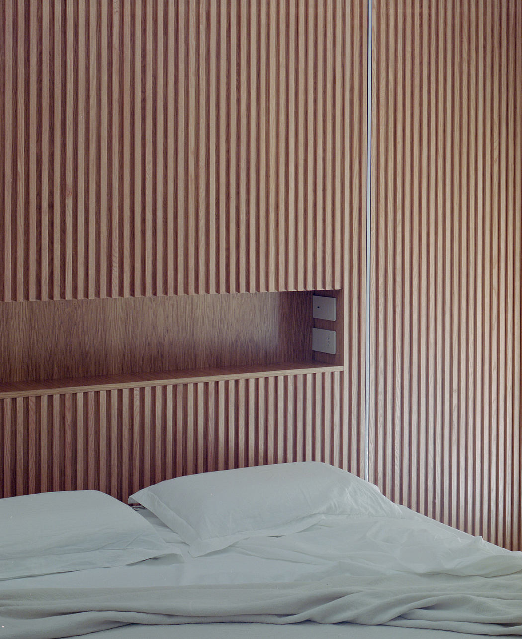 Modern bedroom with vertical wood paneling and unmade bed.