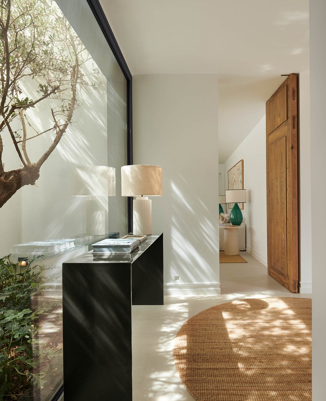 Modern interior hallway with sunlight casting shadows, including a sleek black console and large windows