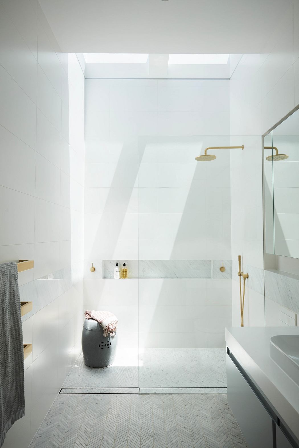 Modern white bathroom with skylight and gold fixtures.