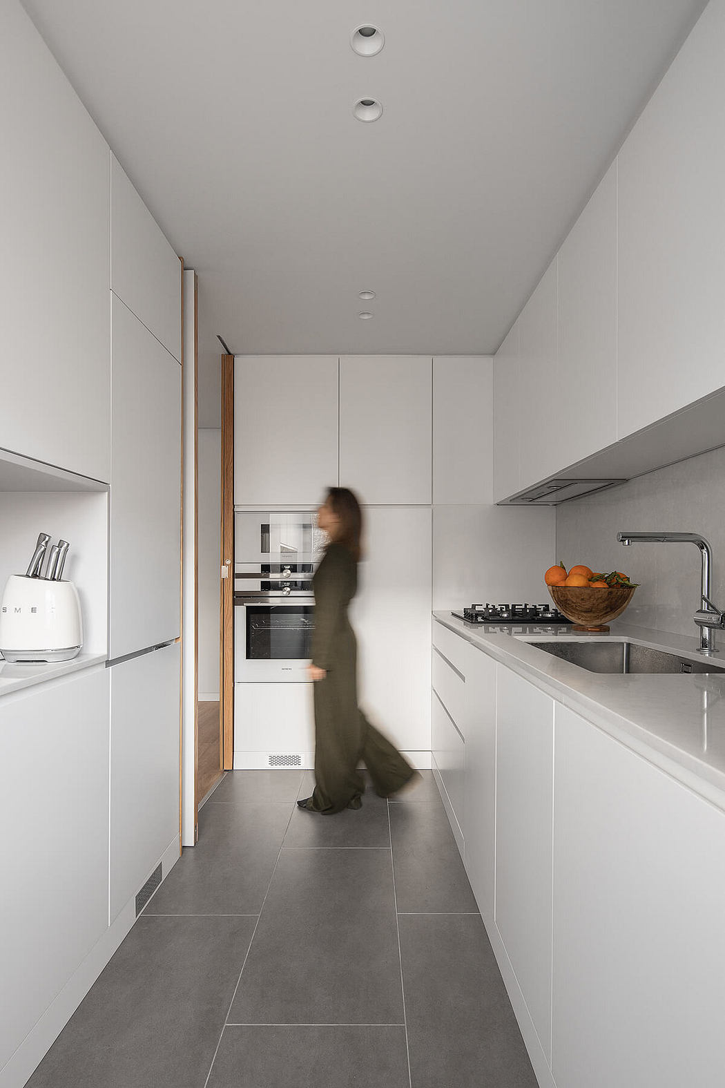 Modern kitchen with white cabinets, stainless steel appliances, and a person in motion.