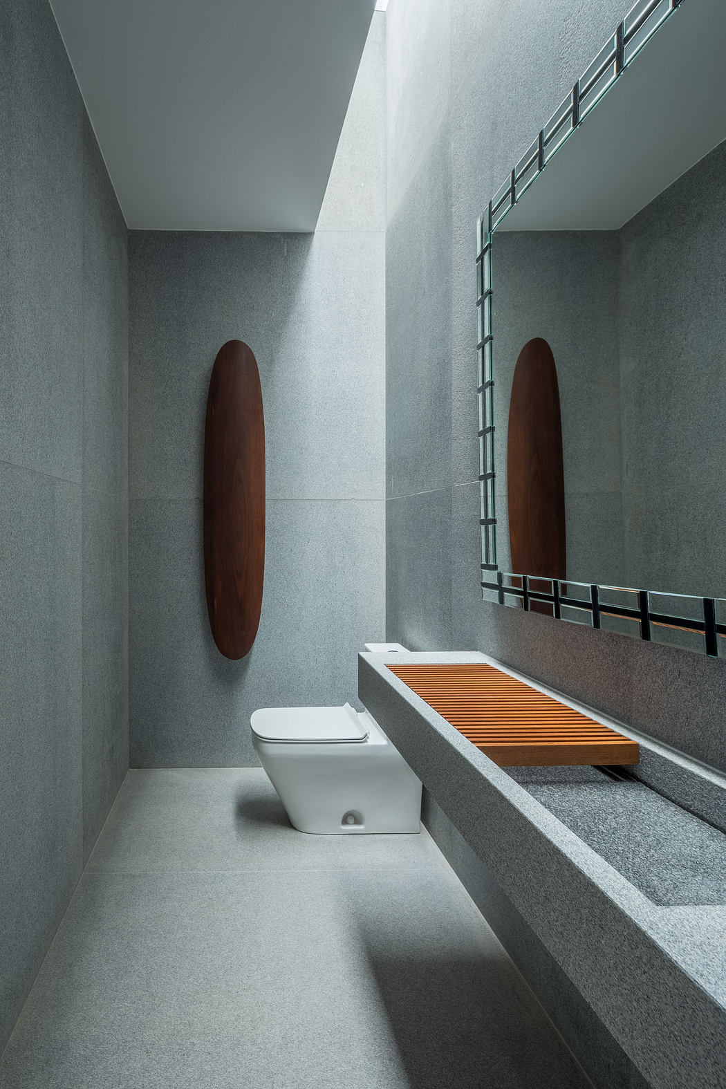 Modern bathroom with gray stone walls, elongated toilet, and wooden bench.
